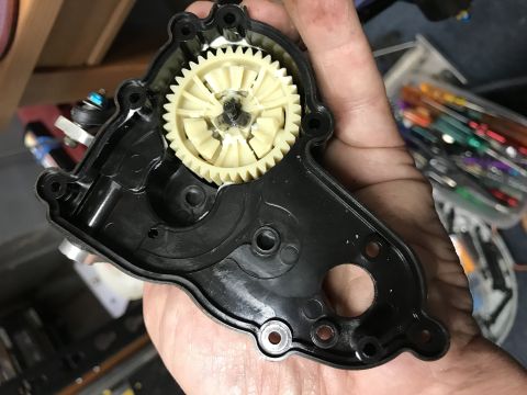 1989 Ford Bronco - A hand holds a disassembled black plastic housing with a yellow plastic gear inside. White sealant is visible around the edges of the housi…