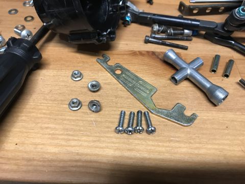 1989 Ford Bronco - A collection of RC car parts and tools are laid out on a wooden surface. Visible items include a screwdriver, various nuts and bolts, a mul…