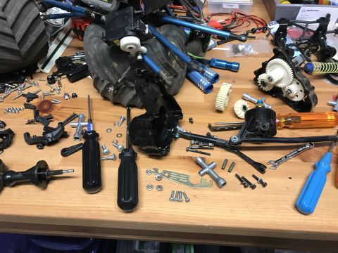 1989 Ford Bronco - A collection of RC car parts and tools are spread across a wooden workbench. Visible parts include gears, suspension components, and variou…