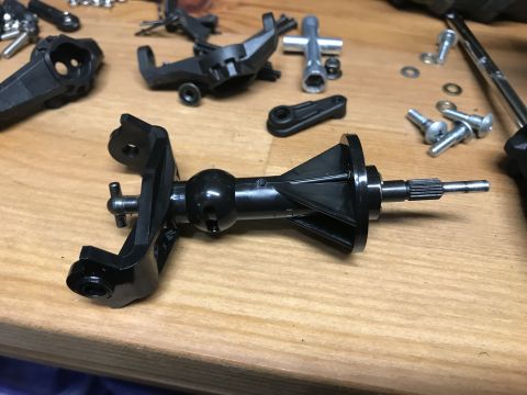 1989 Ford Bronco - A close-up view of disassembled RC car parts, including a differential housing, drive shaft, and various screws and tools, laid out on a wo…