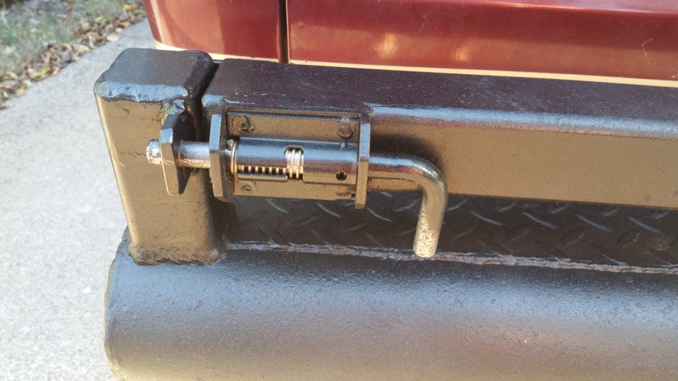 Close-up of a black metal latch with a spring-loaded bolt on a vehicle bumper.