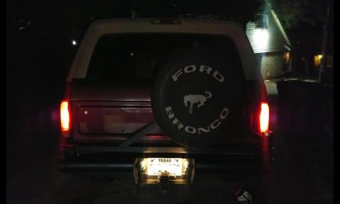 1996 Ford Bronco - The rear of a dark red 1996 Ford Bronco is shown at night, featuring a spare tire cover with the "Ford Bronco" logo and a running horse emb…