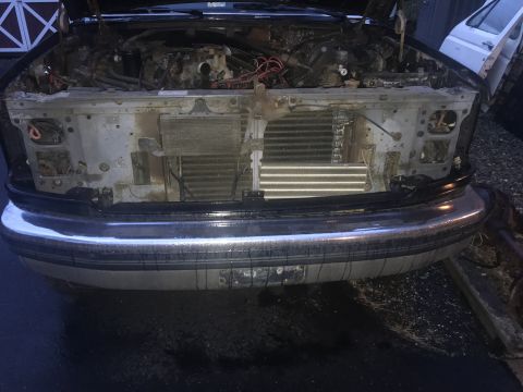 1992 Ford Bronco - Front view of a disassembled vehicle's engine bay, showing the radiator and condenser. The vehicle has a chrome bumper and is parked on a w…