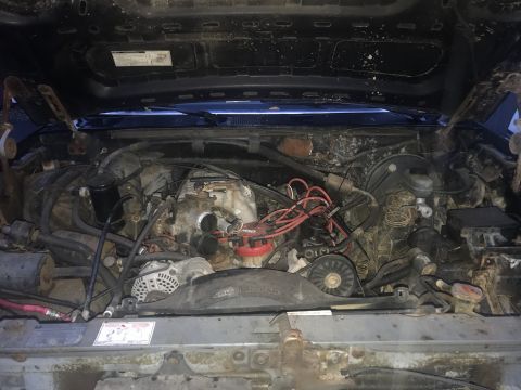1992 Ford Bronco - The engine bay of a 1992 Ford Bronco is shown, filled with various components and wiring. The engine appears dirty and worn, with visible s…