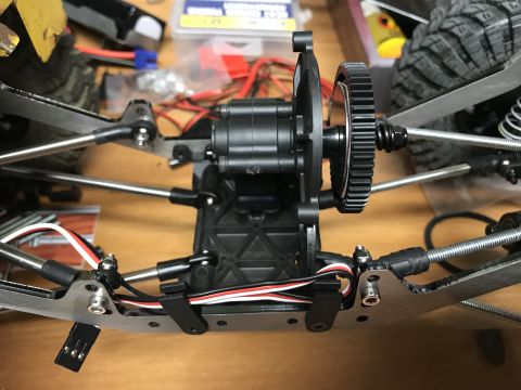 1989 Ford Bronco - Close-up view of the drivetrain and suspension components of an RC car, likely a rock crawler, with visible gears, linkages, and wiring.