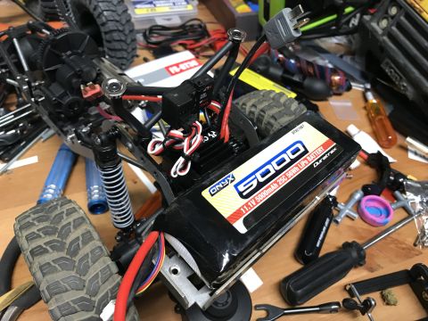 1989 Ford Bronco - A close-up view of a battery pack and electronic components for an RC car, with tools scattered on a wooden surface.