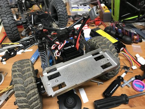 1989 Ford Bronco - A partially assembled RC car chassis with large tires and suspension components is laid out on a wooden workbench with various tools and el…