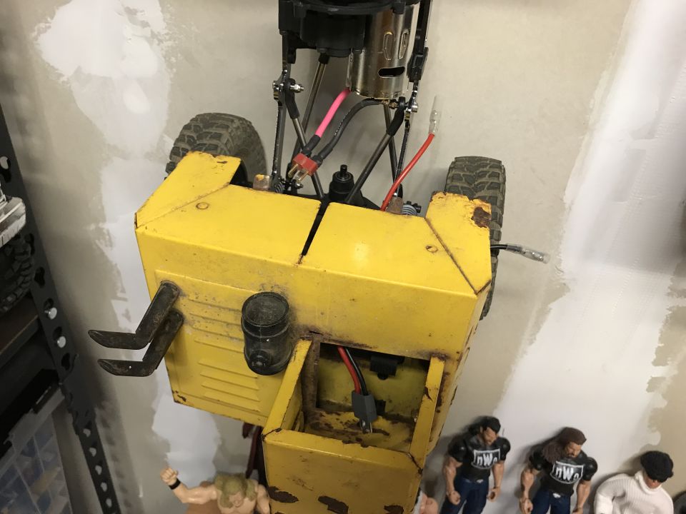 Yellow remote-controlled construction vehicle with toy wrestling figures below.