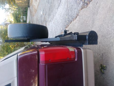 1996 Ford Bronco - A spare tire is mounted on a black rack attached to the rear of a maroon SUV. The rack extends over the rear taillight and has a diamond pl…
