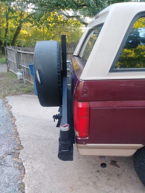 1996 Ford Bronco - The rear driver's side of a maroon and tan Ford Bronco is shown with a spare tire mounted on a swing-away carrier. The vehicle has a tan af…