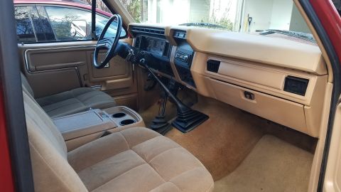 1985 Ford Bronco - The interior of a tan and red 1985 Ford Bronco is shown, focusing on the dashboard, steering wheel, and front seats. The vehicle features a…
