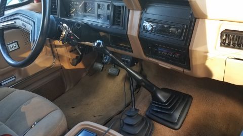 1985 Ford Bronco - The interior of a classic Ford Bronco features a tan dashboard with a manual transmission shifter prominently displayed. The steering wheel…