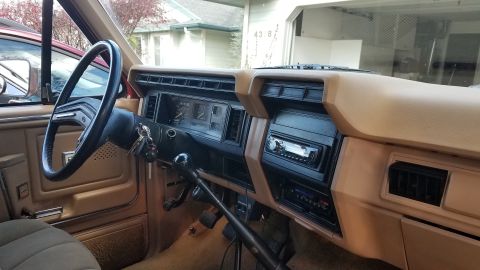 1985 Ford Bronco - Tan interior of an older Ford truck showing the dash, aftermarket radio, column and a long floor-mounted shift lever.