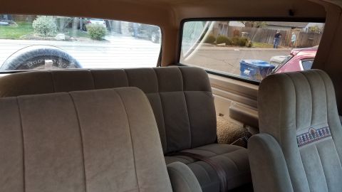 1985 Ford Bronco - Tan cloth front seats inside a vehicle, looking out a side window to a suburban street.