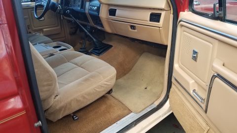 1985 Ford Bronco - The interior of a red Ford truck or SUV is shown, featuring tan cloth seats, a tan dashboard, and a tan floor carpet. The driver's side doo…