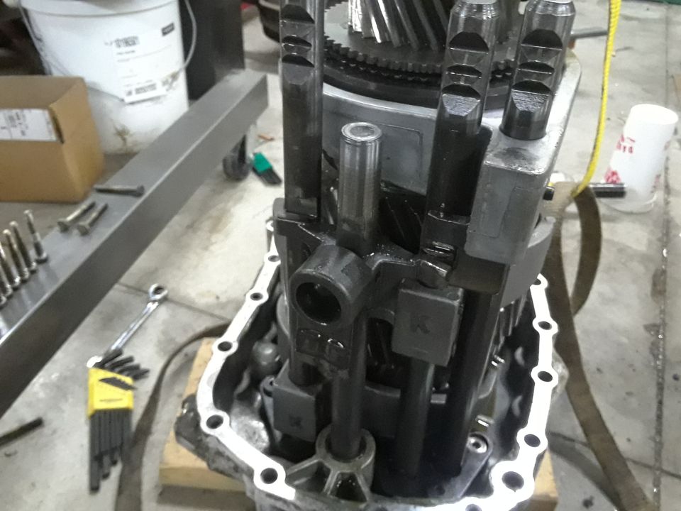 Transmission internal components with levers and gears, and tools on a concrete floor.