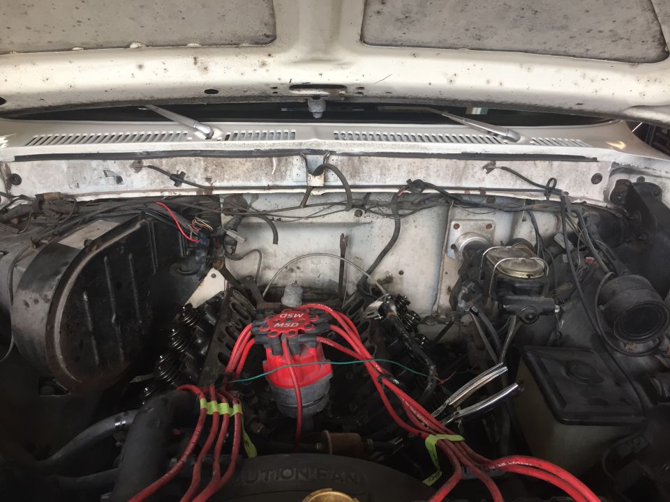 Engine bay of a white vehicle, showing MSD distributor and red spark plug wires.