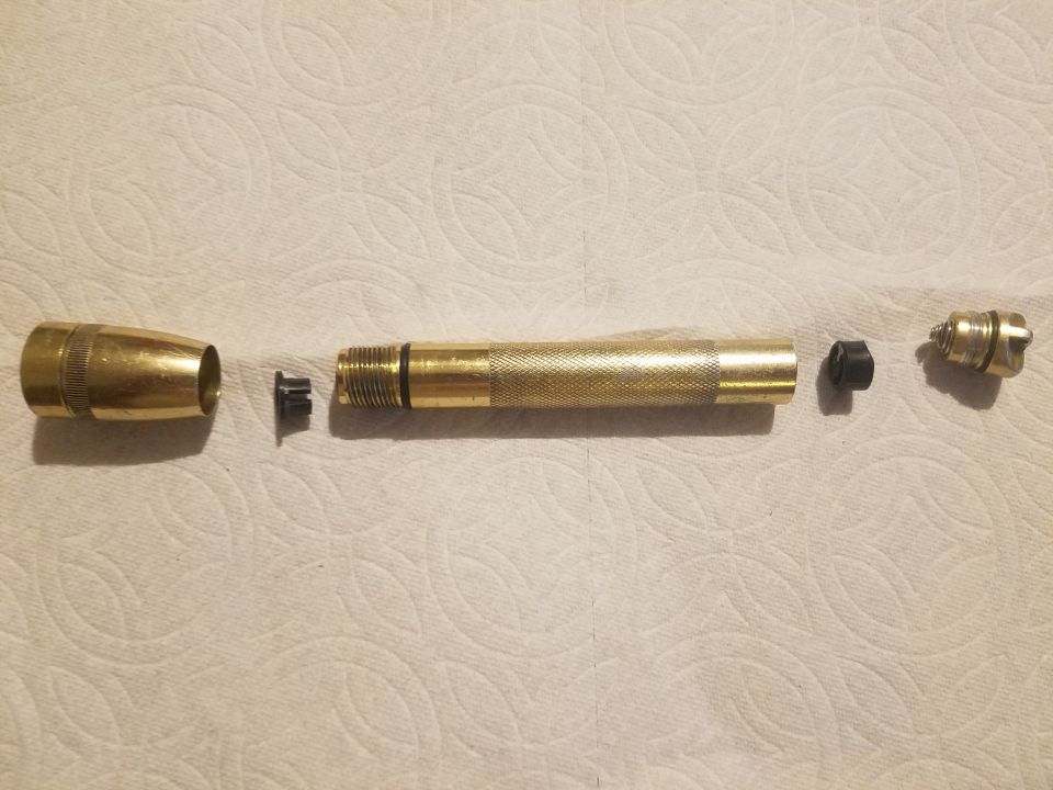 Disassembled brass flashlight on a white paper towel.
