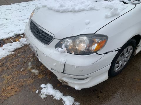 White Toyota Corolla front corner with snow piled on hood and bumper