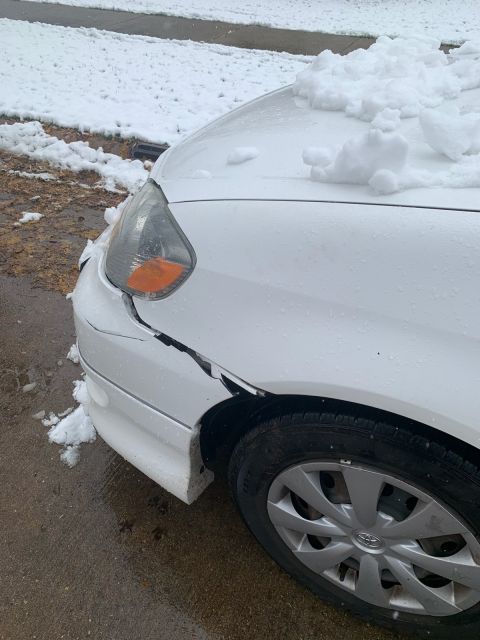 White car front fender cracked and covered in snow, with a damaged headlight