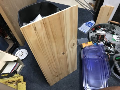 1989 Ford Bronco - A close-up view of unfinished wooden planks leaning against a black trash can, with various parts and containers scattered on a dark blue c…