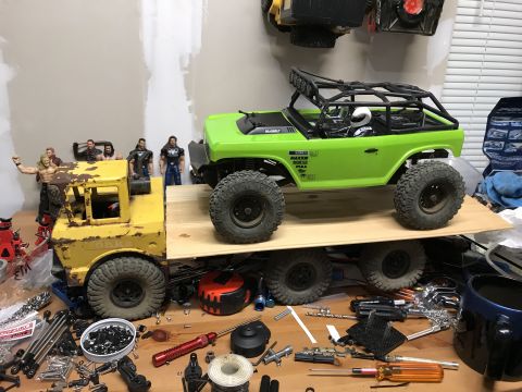 1989 Ford Bronco - A bright green RC rock crawler with a roll cage is parked on a wooden platform, which is elevated by a yellow Tonka toy truck. The scene is…