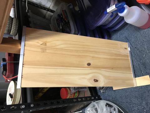 1989 Ford Bronco - A wooden shelf with metal trim sits on a shelf unit. Various items are stored around it, including a spray bottle and containers.