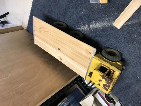 1989 Ford Bronco - A yellow toy truck with a wooden bed is shown on its side on a blue carpet. The truck appears to be a model of a flatbed truck.