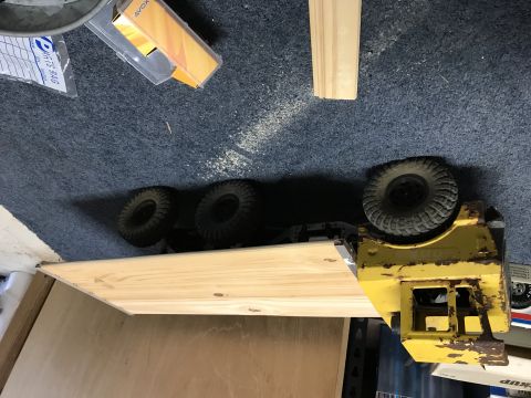 1989 Ford Bronco - A yellow RC truck is shown on its side, resting on a wooden plank. The truck has large, knobby tires and appears to be a model of a utility…