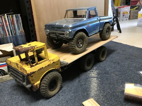 1989 Ford Bronco - A blue RC pickup truck is loaded onto a flatbed trailer pulled by a yellow RC truck. The yellow truck appears rusted and weathered, while t…