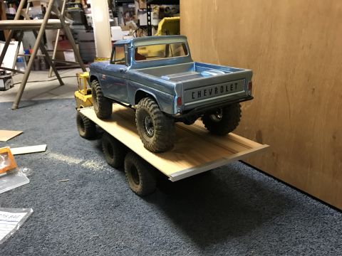 1989 Ford Bronco - A blue Chevrolet pickup truck is loaded onto a flatbed trailer. The truck is a model with large off-road tires and is parked on a carpeted…