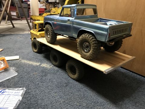 1989 Ford Bronco - A blue Chevrolet pickup truck is loaded onto a wooden trailer with multiple axles. The trailer is being towed by a yellow piece of heavy eq…