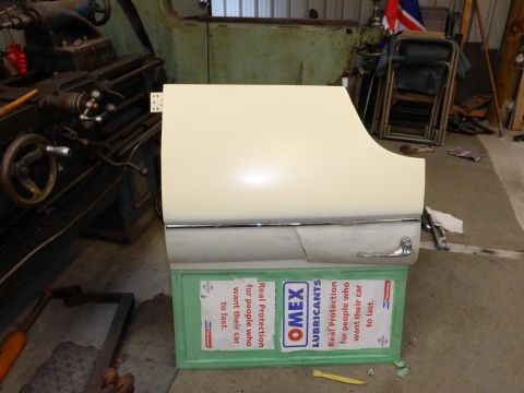 1962 MG B - A car door is shown resting on boxes in a workshop setting, with machinery in the background.