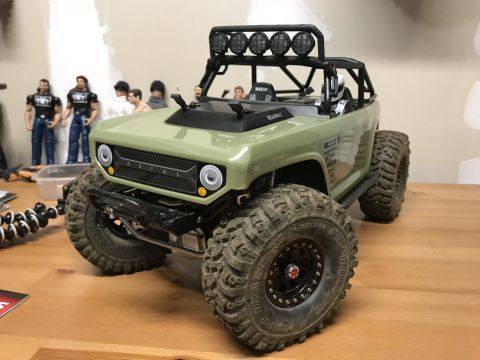 1989 Ford Bronco - A detailed toy RC car sits on a wooden surface, with action figures in the background.