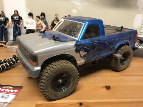 1989 Ford Bronco - A toy truck with custom paint and large tires sits on a wooden surface, with action figures in the background.
