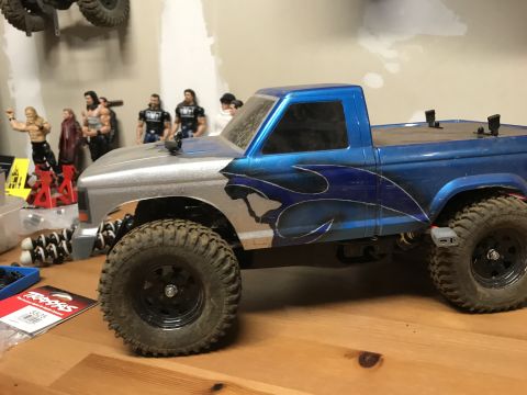 1989 Ford Bronco - A custom-painted RC truck body sits on a wooden surface, with action figures visible in the background.