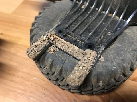 1989 Ford Bronco - Close-up of a dirty RC car tire and a black plastic chassis component.