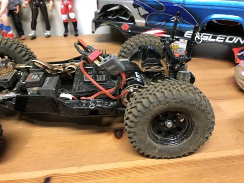 1989 Ford Bronco - The chassis of a remote control car is shown with exposed wiring and large tires, with a blue truck body visible in the background.