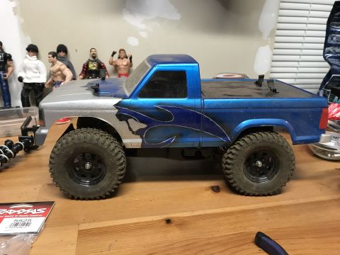1989 Ford Bronco - RC truck with custom flame paint job and off-road tires sits on a wooden surface. A part number is visible in the foreground.