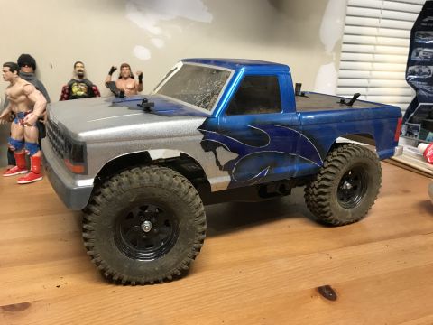 1989 Ford Bronco - A modified remote control truck sits on a wooden surface, with action figures in the background.
