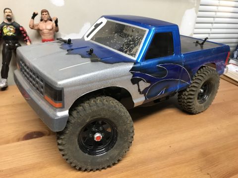 1989 Ford Bronco - A remote-controlled truck with custom paint sits on a wooden surface, with action figures in the background.