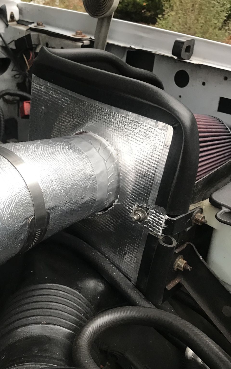 Engine bay shot showing an aftermarket air intake system with silver insulated tubing and a red air filter