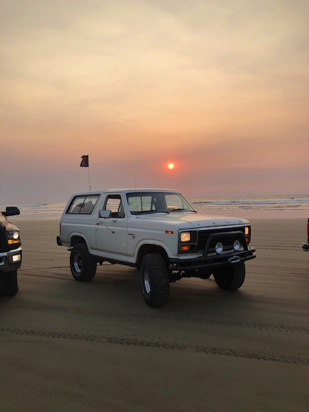 1981 Ford Bronco - White Ford Bronco parked on a beach during sunset, with another vehicle nearby.