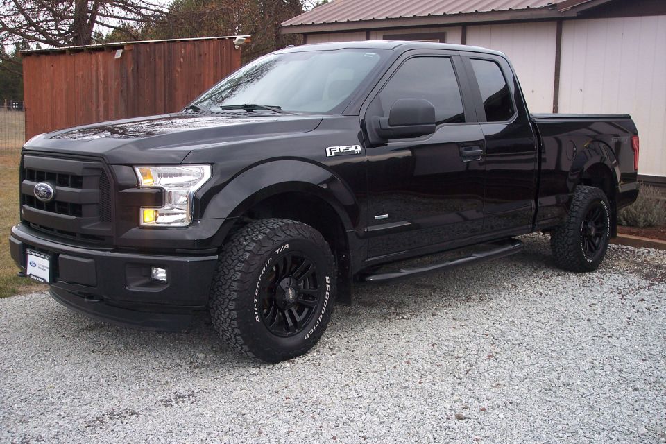 Black Ford F-150 pickup truck with aftermarket wheels and tires parked on gravel.