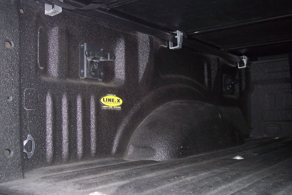 Black Line-X sprayed truck bed interior with tonneau cover rails and tie-downs.
