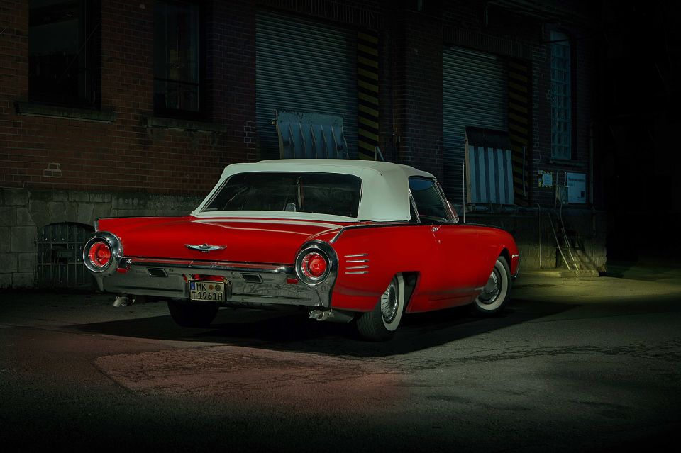 Red 1961 Ford Thunderbird convertible with white top, rear-left view, parked at night.