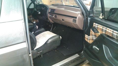 1992 Ford Bronco - The interior of a dark-colored SUV, likely a Ford Bronco, is shown from the driver's side door. The interior features tan plaid fabric acce…