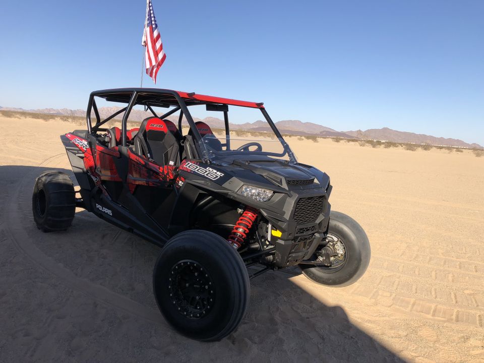 Black and red Polaris RZR 1000 UTV with American flag on a sand dune.