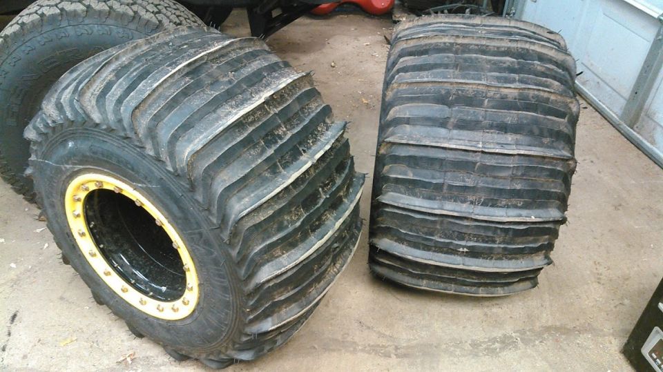 Two large off-road tires, one on a yellow-beadlock rim, on a concrete floor.