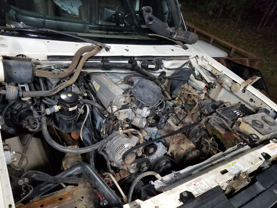 Engine bay of white Ford Bronco with V8 engine, intake tube removed and resting on cowl